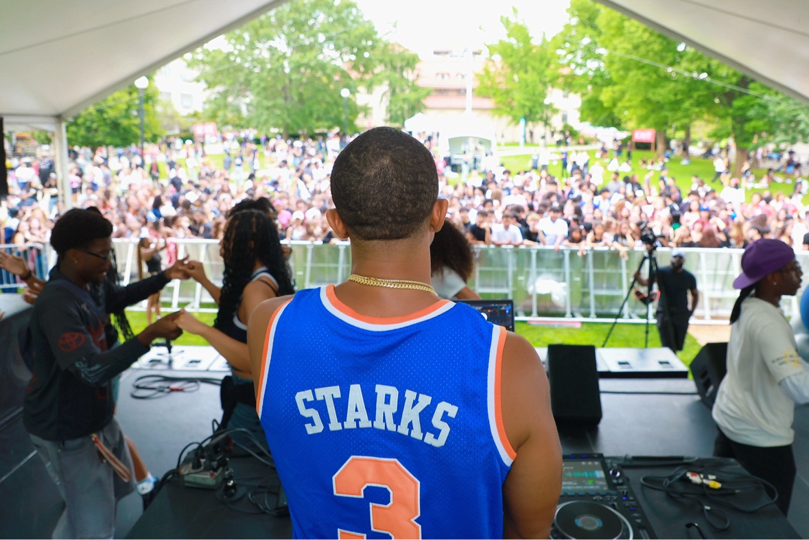 DJ Takeova at the decks facing a packed outdoor festival crowd