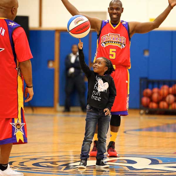 A child spinning a basketball while Harlem Wizards players cheer