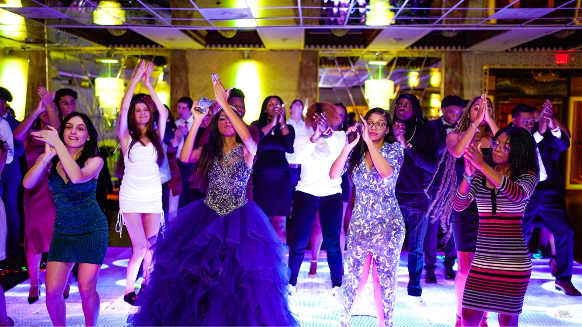 Students in formal wear dancing together on a lit ballroom floor at prom
