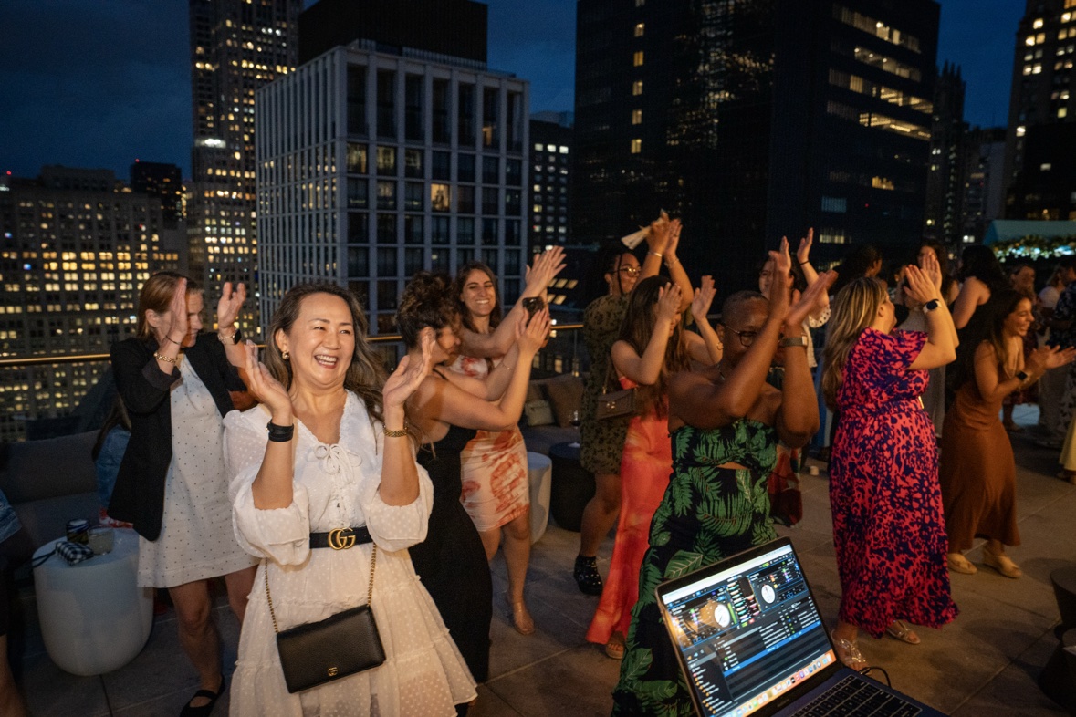 Guests dancing at a private rooftop party at dusk with the New York City skyline behind them